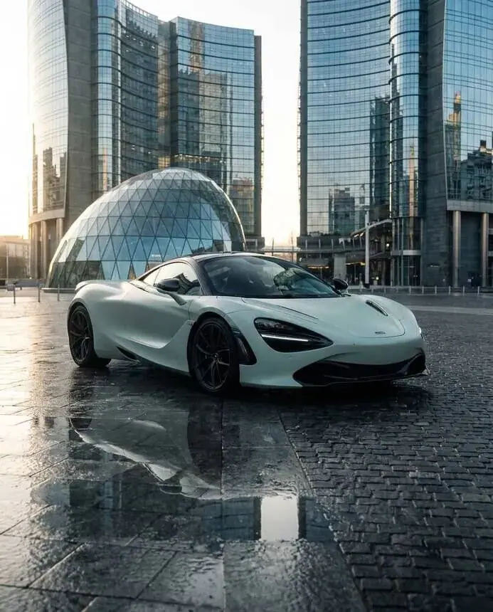 Car campaign imagery: white supercar in a city of glass towers after rain